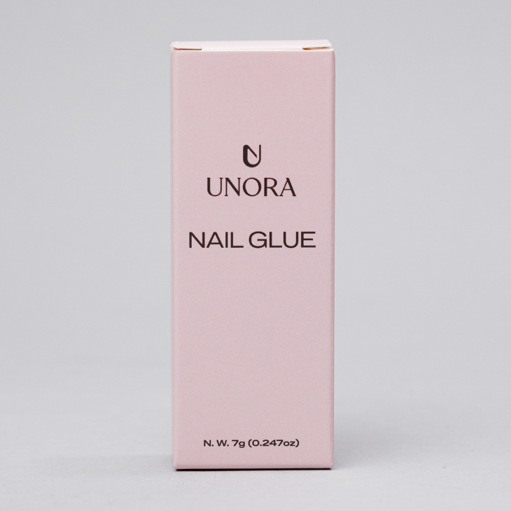 A tall, light pink rectangular box of UNORA Nail Glue, standing upright against a neutral light gray background.