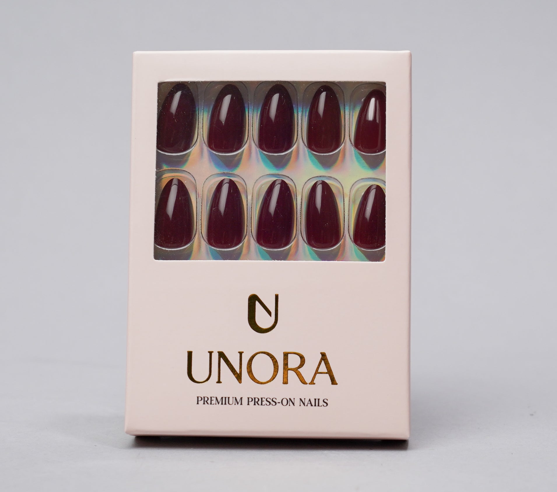 A box of UNORA premium press-on nails with a clear window showing almond-shaped nails in a deep burgundy color, set against a neutral gray background.