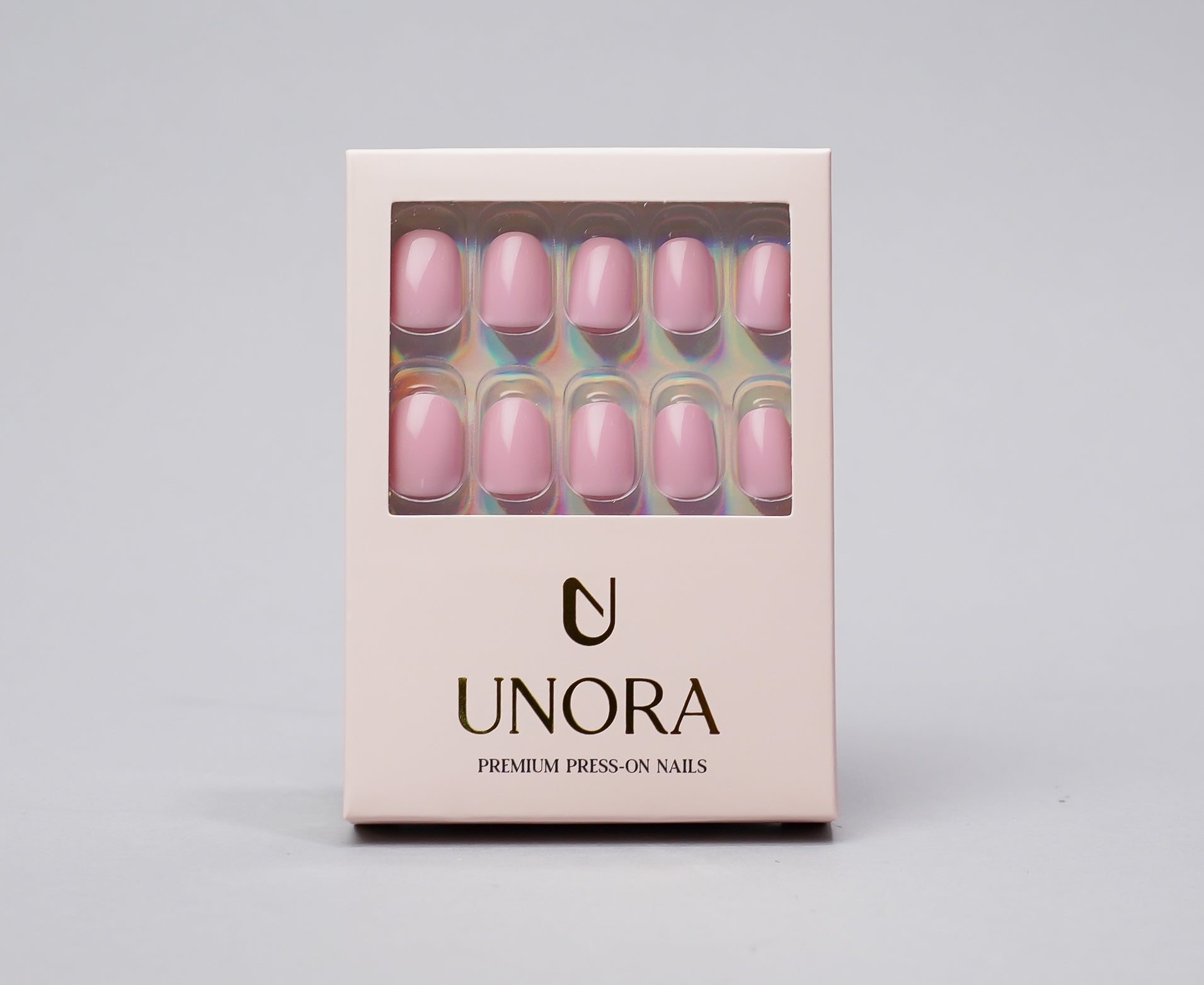 A boxed set of press-on nails by UNORA, featuring a pale pink window display showing the nails inside, with the brand name printed below on a light pink box against a neutral gray background.