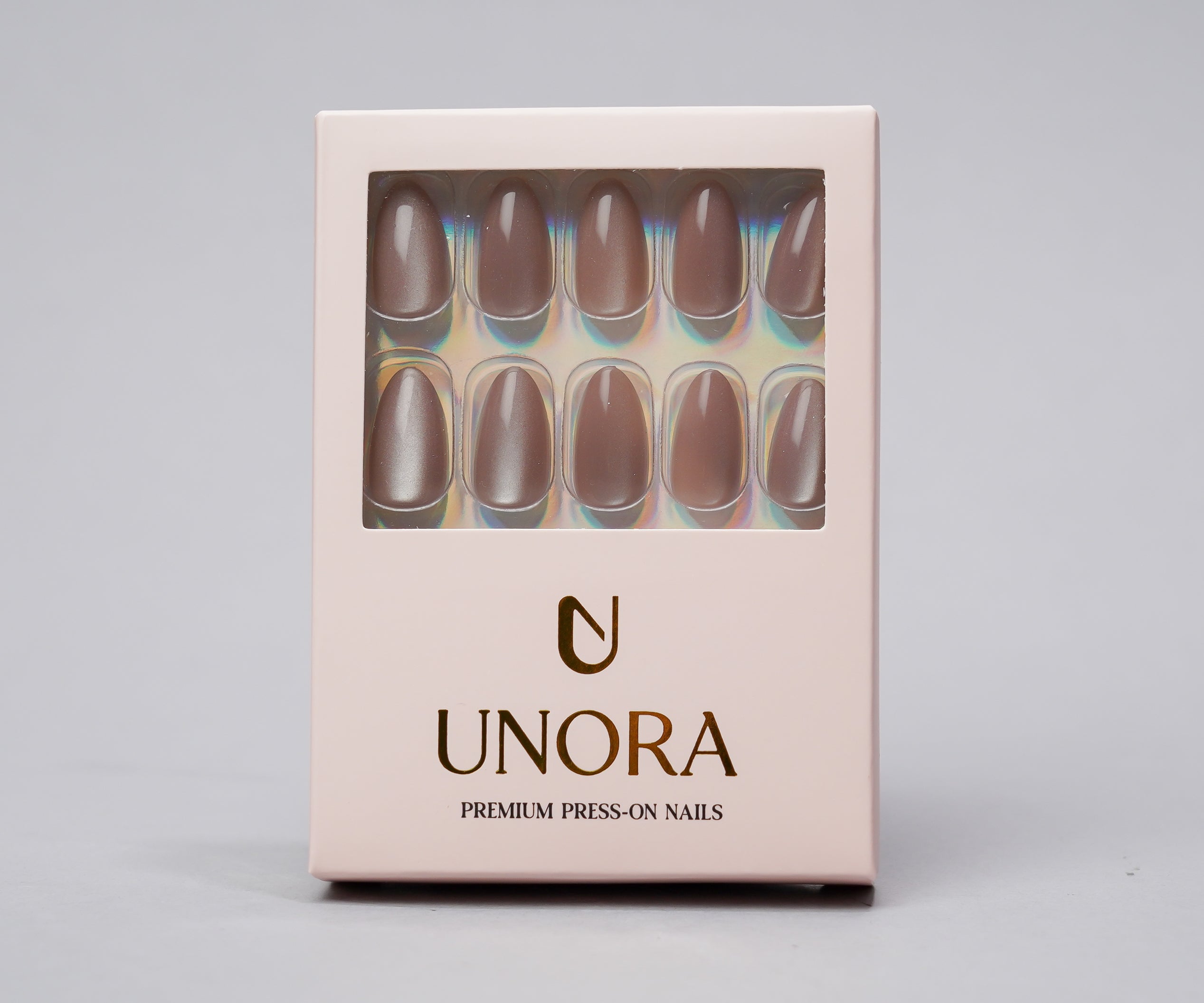 UNORA brand press-on nail set in a light pink rectangular box with a clear window showing glossy nude-brown nails, photographed on a neutral gray background.