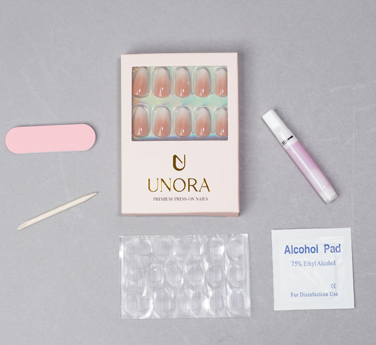 UNORA press-on nail kit arranged on a light gray background, including a box of nude-pink press-on nails, a pink nail file, a wooden nail tool, a pink gel polish tube, a clear nail file sheet, and an alcohol pad.